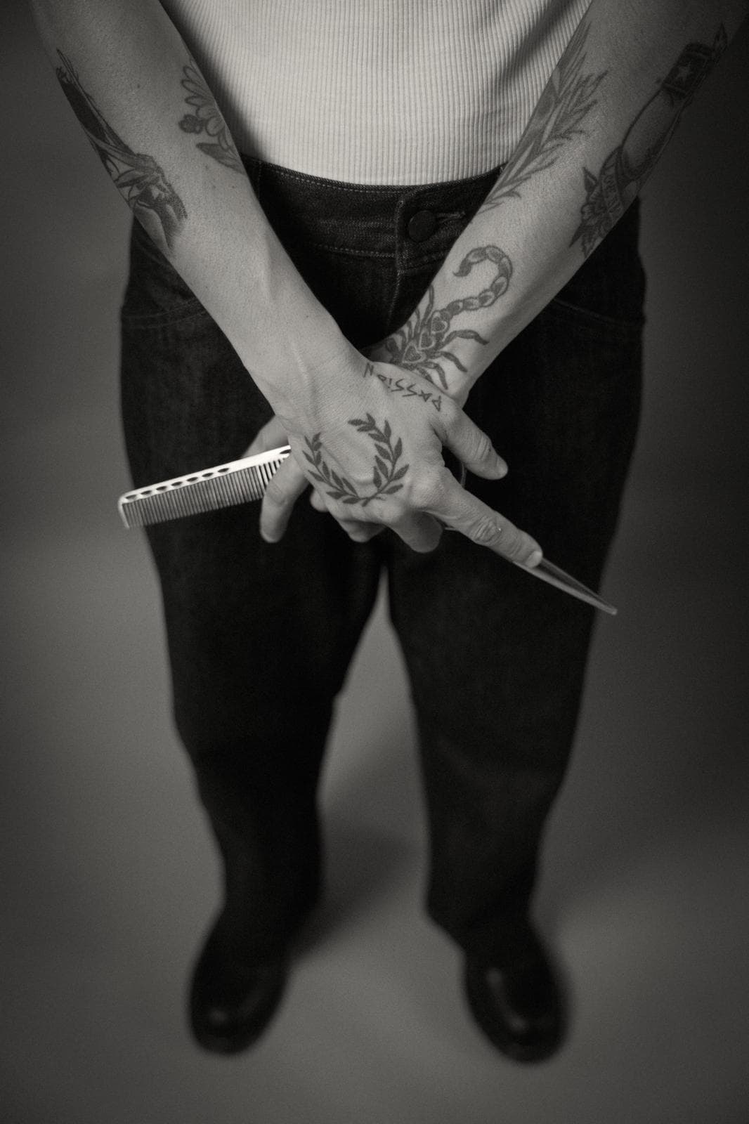 Manos tatuadas sujetando un peine y unas tijeras
