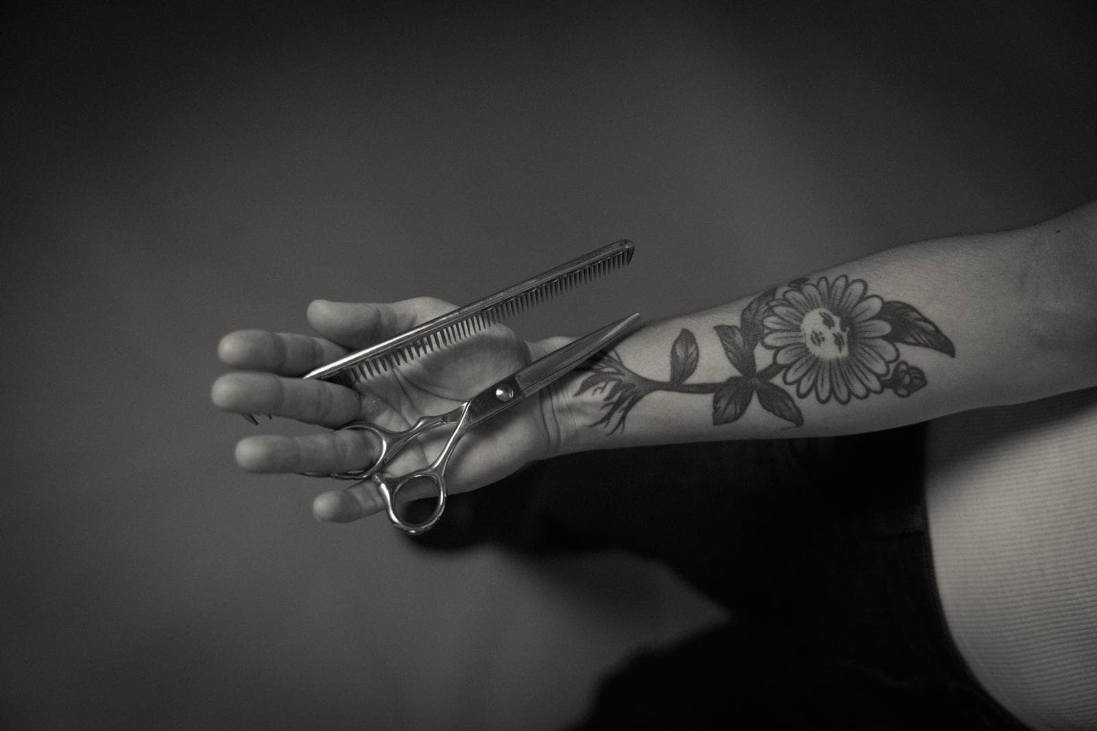 Mano tatuada sosteniendo tijeras y peine